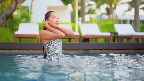 A-passionate-sensual-young-Asian-woman-touches-her-wet-hair-in-the-swimming-pool-of-an-exotic-hotel-on-the-lounge-background