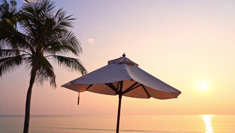Beach-umbrella-and-coconut-palm-tree-silhouette-on-colorful-golden-sunset-in-Thailand