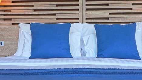 Made-up-clean-bed-with-blue-pillows-and-linen-striped-cover-at-hotel-in-the-Philippines,-Slow-panning-right
