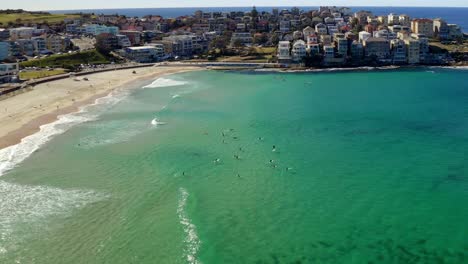 Surfers-Surfing-At-Clear-Blue-Water-Of-Sea-Near-Bondi-Beach-With-Ben-Buckler-Suburb-In-The-Distance