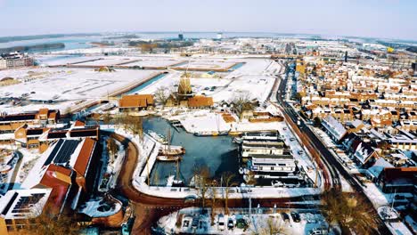 Snow-Covered-Harderwijk-Town-in-Netherlands,-Drone-View-on-Sunny-Day,-Bird-Passes-Frame