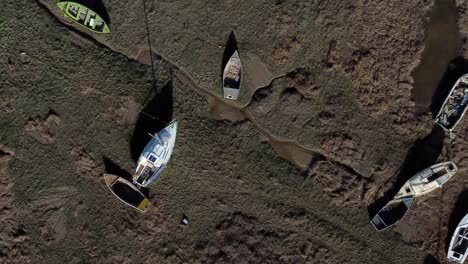 Aerial-view-over-various-stranded-abandoned-fishing-boat-wreck-shipyard-in-marsh-mud-low-tide-coastline