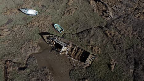 Abandoned-weathered-wooden-fishing-boat-wreck-shipyard-in-marsh-mud-low-tide-coastline-aerial-view-rising