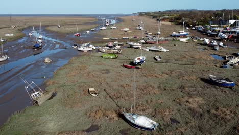 Various-stranded-abandoned-fishing-boat-wreck-shipyard-in-marsh-mud-low-tide-coastline-aerial-view-pull-back