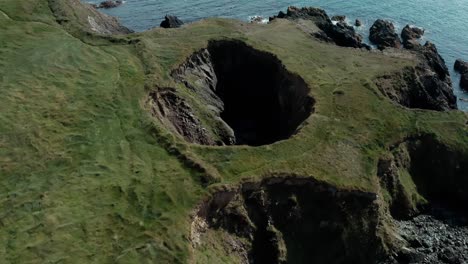 Aerial-orbiting-shot-or-small-crater-near-seaside-cliff-at-day