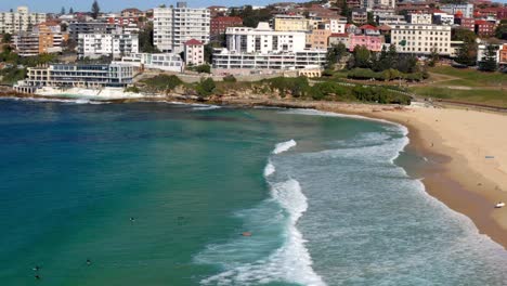 Beachgoers-Swimming-And-Surfing-At-Bondi-Beach-With-Oceanside-Swimming-Pool-And-Buildings-In-Background
