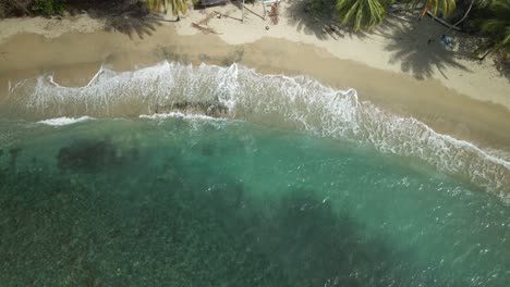 Ascending-aerial-view-of-waves-crashing-on-the-shoreline-of-an-amazing-crystal-clear-water-beach-in-Arnos-Vale,-Tobago