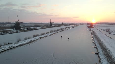 Atemberaubender-Sonnenaufgang-Mit-Paar-Eislaufen-Auf-Dem-Fluss-Bei-Kinderdijk-Windmühlen