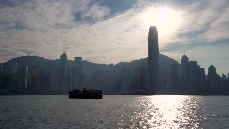 Beautiful-famous-Hong-Kong-Mega-City-Skyline-silhouette,-historical-Star-Ferry-boat-sailing-across-Victoria-Sea-Harbor-on-Hot-Sunny-Blue-Sky-Summer-Day,-bright-sun-shining,-reflecting-on-water