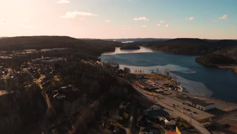 Aerial-drone-shot-of-rural-city-located-beside-beautiful-lake-during-sunset