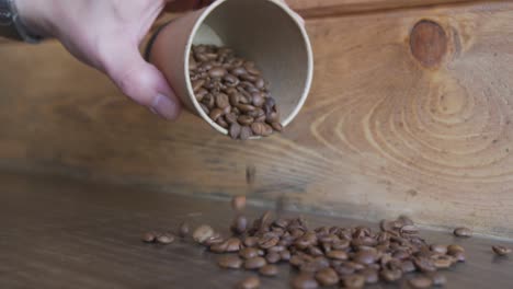 Hand-Spilling-Coffee-Beans-In-A-Cup-Onto-Wooden-Table