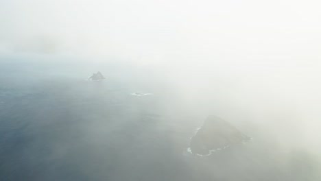 Mysterious-islands-in-blue-atlantic-ocean-with-thick-clouds-and-mist,-aerial