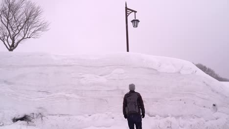 Male-tourist-walking-up-to-very-high-snow-wall-in-Aomori,-Japan