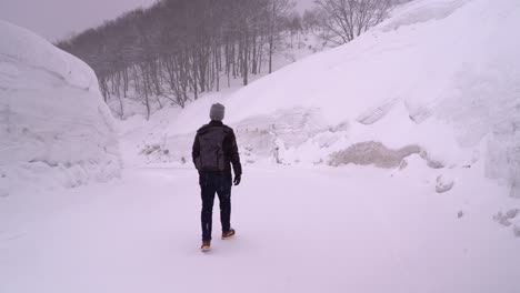 Male-tourist-walking-through-snowed-in-Landscape-with-high-snow-walls-in-Japan