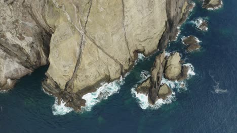 Jagged-cliffs-with-blue-ocean-water,-volcanic-rock-island-in-Atlantic,-aerial