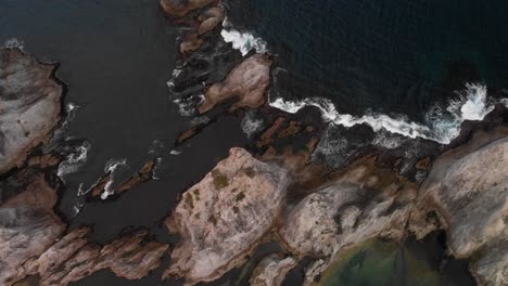 Top-down-aerial-over-tall-cliffs-with-breaking-waves-during-rough-weather