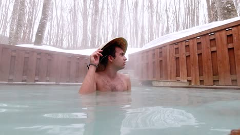 Foreign-male-tourist-wearing-straw-hat-inside-open-air-Onsen-with-snow-in-Japan