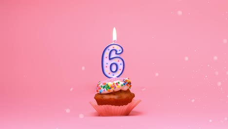 Close-up-of-a-Happy-Birthday-celebration-cupcake-with-frosting,-sprinkles-and-a-lit-up-6-years-old-candle-flame-burning-and-moving-around-on-a-pink-coral-background---seamless-boomerang-loop