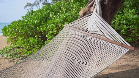 Empty-hammock-net-bed-hanging-on-a-tree-on-a-sunny-tropical-beach,-exotic-travel-concept,-close-up