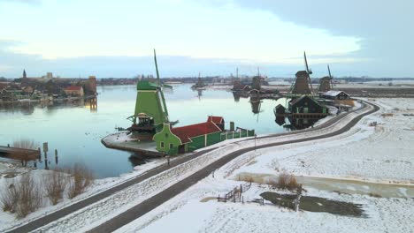Person-running-next-to-iconic-Dutch-windmills-during-winter-season,-aerial