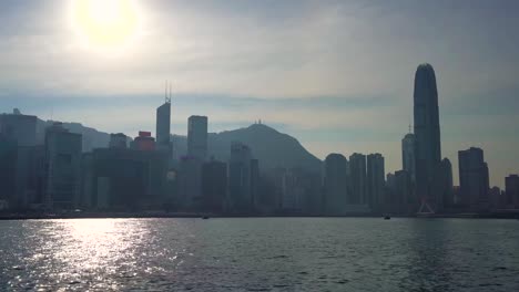 Schöne-Berühmte-Hong-Kong-Mega-City-Skyline-Silhouette,-Segeln-über-Den-Victoria-Sea-Hafen-Auf-Einem-Boot-An-Heißen-Sonnigen-Sommertagen-Mit-Blauem-Himmel,-Helle-Sonne,-Die-Auf-Wasser-Reflektiert
