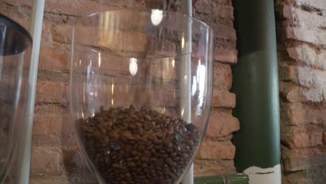 Beutel-Mit-Frisch-Gerösteten-Kaffeebohnen-In-Ein-Glasgefäß-Auf-Der-Kaffeemühle-Gießen