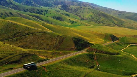 Following-a-cargo-truck-through-the-foothills-of-the-Tehachapi-Mountains-at-spring-with-unusually-green-landscape---aerial-parallax-view