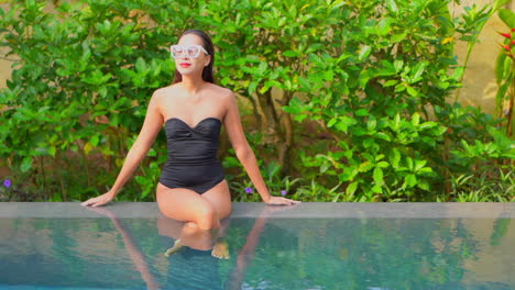 Asian-girl-sitting-on-pool-edge-with-black-swimsuit-and-vintage-sunglasses