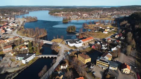 Ascend-aerial-top-down-showing-frozen-lake-surrounded-by-small-city-buildings-in-Bengtsfors,-Sweden