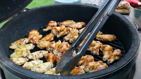 Tongs-flipping-chicken-wings-with-BBQ-sauce-cooking-on-a-kamado-style-ceramic-grill