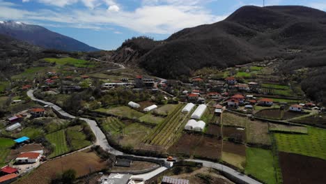 Village-on-beautiful-hills,-greenhouses,-agricultural-parcels-and-mountains-background-in-Albania