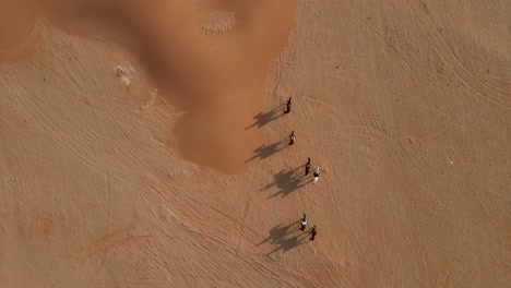 UAE:-Aerial-view-of-a-group-of-tourist-riding-on-Arabian-horses-walking-in-the-desert-of-Mleiha,-United-Arab-Emirates