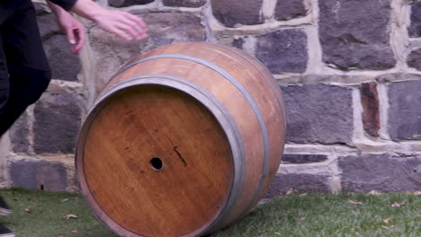 Rolling-a-wine-wooden-barrel-across-green-grass-past-a-stone-wall