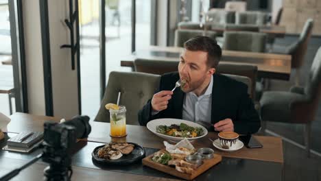 A-handsome-young-man-evaluates-a-salad-in-a-restaurant-and-shoots-everything-on-a-video-camera