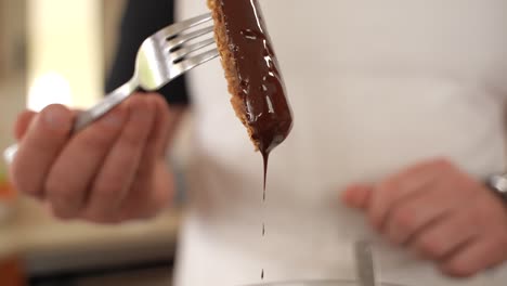 Chef-in-White-Shirt-Shakes-Oatmeal-Bar-on-Fork,-Chocolate-Dripping-in-Slow-Motion
