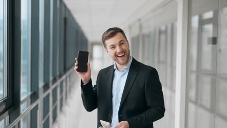 Handsome-young-man-in-business-suit-shows-smartphone-and-money