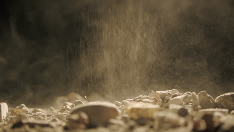 Macro-shot-of-Falling-dust-and-rocks-on-surface-with-Black-background,-slow-smooth-dolly