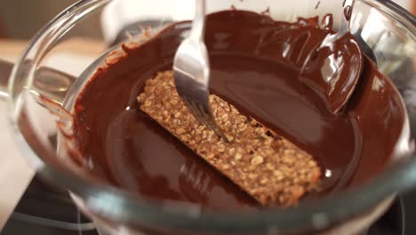 Dipping-Healthy-Homemade-Oatmeal-Bar-in-Melted-Chocolate,-Close-Up