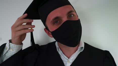 Porträt-Eines-Glücklichen-Absolventen,-Der-Eine-Schutzmaske-Aufsetzt,-Robe-Und-Abschlusskappe-Trägt
