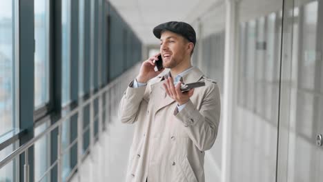 Cheerful-adult-man-talking-on-the-phone-in-a-glass-corridor