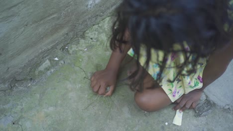Young-Indian-poor-orphan-girl-playing-with-stone-on-ground,-rural-village