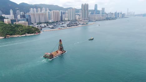 Tugboat-pulling-a-barge-loaded-with-fresh-excavated-Sand-along-Hong-Kong-coastline,-Aerial-view