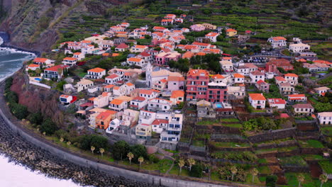 Aerial-view-of-small-village-with-beautiful-houses-on-crashing-waves-against-shore-on-coastline