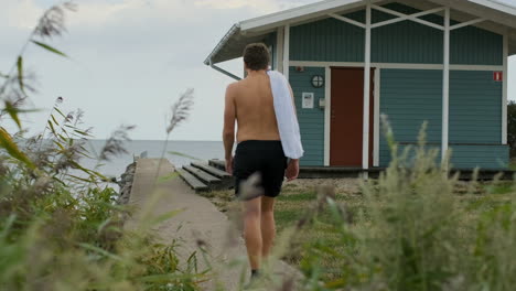 Walking-man-with-towel-runner-athletic-going-for-swim-cold-sea-water-beach-cabin-cool-down-cloudy-day-sauna-spa-relaxing-relax-runner-running-athlete-training-triathlon-lonely-alone-guy-sneakers-trunk