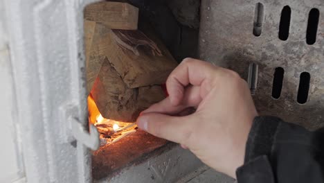 Man-lights-a-match-and-tries-to-light-firewood-in-old-home-tiled-stove,-then-closes-the-door