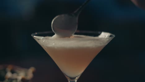 Close-up-of-classy-alcoholic-cocktail-in-glass-and-spoon-aligning-foam-selective-focus,-slow-motion