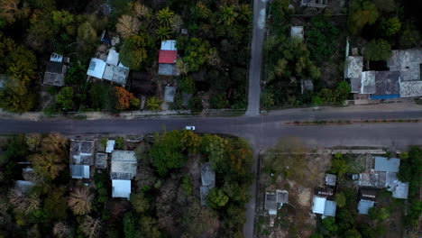 Downward-angle-drone-shot-following-white-car-driving-through-streets-of-Merida-Mexico
