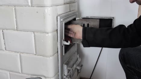 Man-puts-the-firewood-into-old-home-tiled-stove-and-closes-the-door