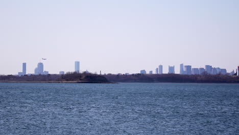 Distant-view-of-Boston-Skyline,-aircraft-coming-into-frame-from-left-to-land-at-Boston-International-Airport