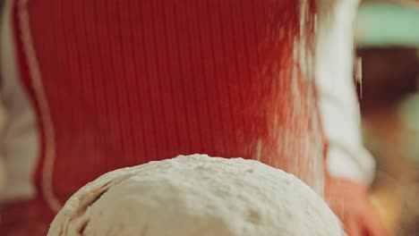 Extreme-Close-up-shot-of-applying-flour-on-the-dough-by-a-woman-chef-in-a-red-apron